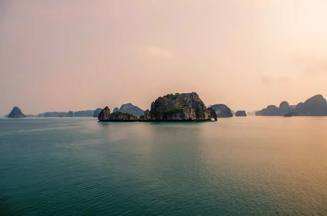 Isolated limestone island in calm Halong Bay waters at sunset