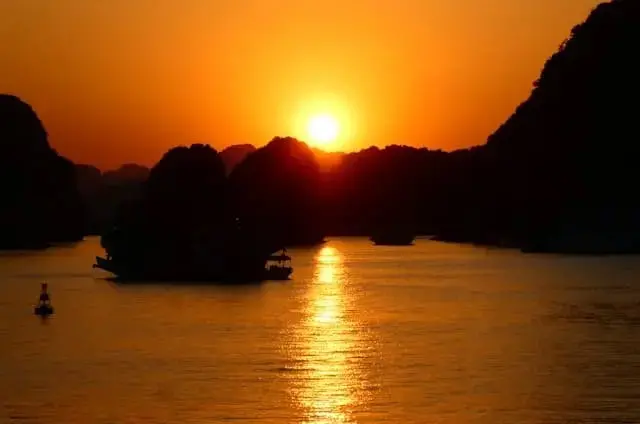 Golden sunset reflecting on Halong Bay waters with silhouette of boats